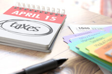 April 15 daily calendar with taxes circled on desk with colorful tax category folders and window light