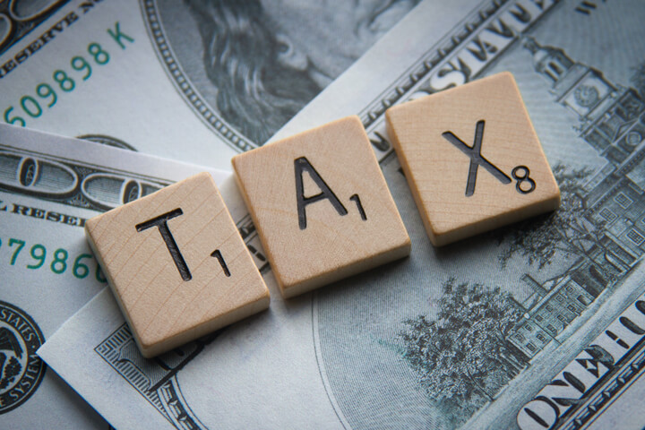 Tax Scrabble letters on scattered 100 dollar bills