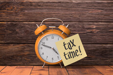 Alarm clock with tax time sticky note Orange alarm clock with yellow sticky note reading tax time
