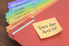 Tax folders with sticky note reminder Rainbow-colored tax category folders with sticky note to remind taxes due April 15