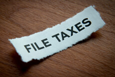 Torn piece of paper with the text File Taxes printed on it with vignette on wood background