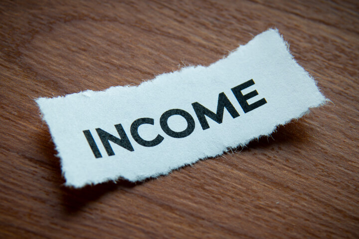 Torn piece of paper with word Income on depth of field and vignette on wood surface