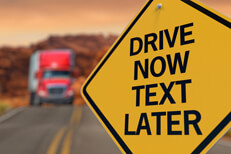 Road sign reading drive now text later with large semi burred in distance