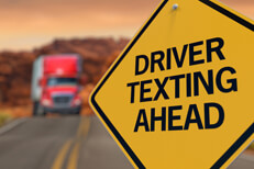 Driver texting ahead sign Yellow road sign reading Driver Texting Ahead with oncoming semi truck in blurred in background