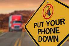 Traffic sign put your phone down Road sign with Put Your Phone Down and no texting icon with oncoming semi truck on highway in background